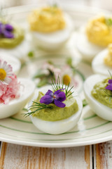 Fototapeta na wymiar Deviled egg stuffed with avocado, decorated with fresh dill and edible violet