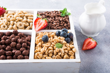 Milk jug and variety of cold quick breakfast cereals with berries in white wooden box, healthy eating concept, selective focus.
