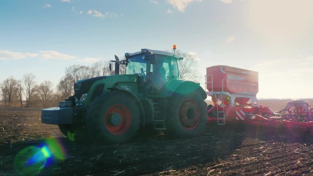Steadicam fly around shot: A tractor with a large seeder is driving across the field in the sun.