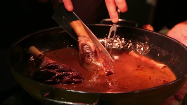 Pork shank in juicy sause slicing and serving in restaurant