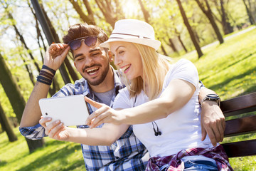 Couple sitting on bench and taking selfie on beautiful sunny day