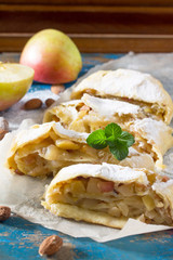 Homemade apple strudel with fresh apples, nuts and powdered sugar on a blue vintage wooden background. Country style apple strudel.