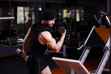 Strong healthy adult ripped man with big muscles training with dumbbells in gym