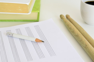 Drum sticks, a pencil and a music sheet next to some books and a cup of coffee on a desk in a classroom. Empty copy space for Editor's text.