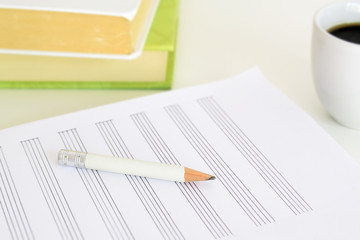 A pen and a music sheet next to some books and a cup of coffee on a desk in a classroom. Empty copy space for Editor's text.