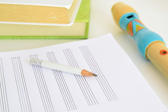 A Flute, A Pencil And A Music Sheet Next To Some Books On A Desk In A Classroom. Empty Copy Space For Editor's Text.