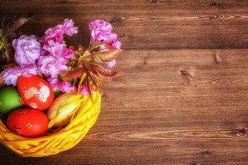 Easter composition - eggs in a basket decorated with sakura blooming branch on wooden background with copy space