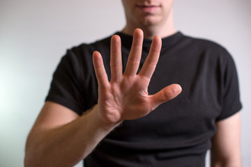 Serious young man showing stop gesture isolated on gray wall background