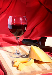 Bottle and Glass with red wine grapes and chees on wooden table.