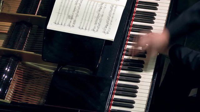 Pianist plays open piano at a classical music concert. Music sheets of VII century classics (now public-domain). Hands and keyboard close-up.