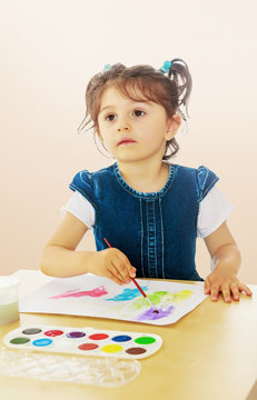 Little girl paints with watercolors at the table.