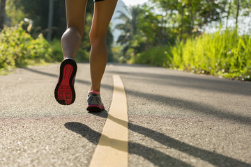 Young fitness woman runner legs running on morning tropical forest trail