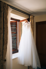 Fototapeta na wymiar The bride's dress hangs on the cornice on the window.