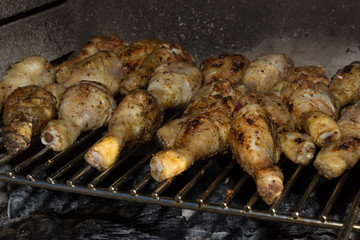 Golden brown chicken legs thighs on a grill with a lit fire barbecue