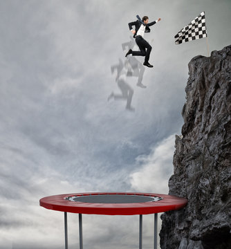 Businessman Jumping On A Trampoline To Reach The Flag. Achievement Business Goal And Difficult Career Concept