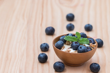 Yogurt with granola and organic blueberries in wooden bowl.