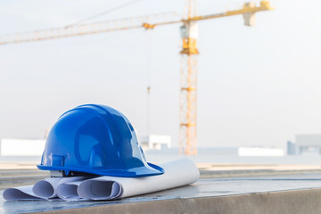 The blue safety helmet put on the blueprint at construction site with crane background