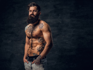 Obraz na płótnie Canvas Bearded male with tattooed torso posing over dark grey background.