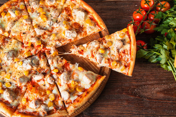 Hot delicious pizza with chicken, cheese and corn with cut piece served on rustic wooden table with...