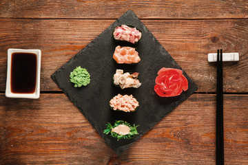 Fresh delicious set of five gunkan sushi served on black slate with ginger and wasabi, on wooden rustic table, flat lay. Tasty seafood, gourmet delicacy. Japanese cuisine.