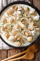 Tasty clams in a creamy sauce with garlic and greens close-up on a table. Vertical top view