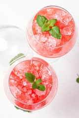 Strawberry cocktail with ice and mint leaves in wine glasses close-up view from above on a white background.