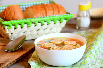 Diet soup with vegetable mix and fried omelet in a bowl. Bread slices, spoon on a rustic wooden background. Healthy soup with omelet, carrot, peas, leek, cauliflower and potatoes