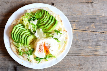 Poached egg, fresh avocado, salad, chinese cabbage, spices, sauce on a flour tortilla. Homemade tortilla with vegetarian filling on a plate isolated on old wooden background with copy space. Top view
