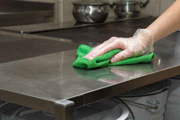 Hand in protective glove with rag cleaning kitchen equipment in the professional kitchen. Stainless steel surface. Early spring cleaning or regular clean up. - obrazy, fototapety, plakaty