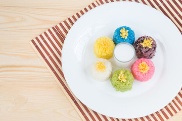 Sweet coconut sticky rice in many colours, Thai sweets for serving with fresh sliced mango, with coconut milk on bamboo place mat over wooden table