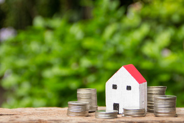 Coins and miniature house on wooden table and blurred of garden background.