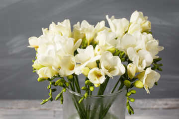 White freesia flowers in decorative vase on a background of gray wall