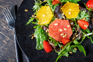Grapefruit and orange mix salad with pine nuts on black plate and dark background