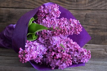 Lilac flowers bouquet in purple paper on wooden background