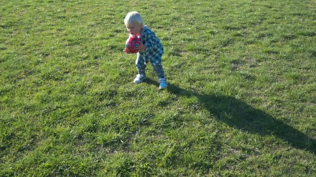 One and a half year old boy joyfully chases the ball on the field