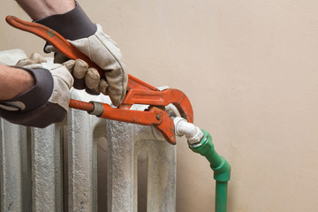 Man's hand in protective glove working with an adjustable wrench at old radiator. Plumbing.