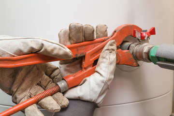 Man's hand in protective glove working with an adjustable wrench at water heater boiler. Plumbing.