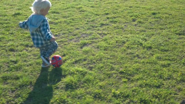 One and a half year old boy joyfully chases the ball on the field