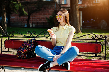 Fototapeta na wymiar Young teenage girl sitting on bench with ice cream at hands, wear on yellow t-shirt, jeans and sunglasses.