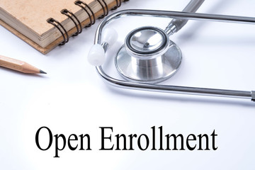 Stethoscope on notebook and pencil with Open Enrollment words as medical concept.
