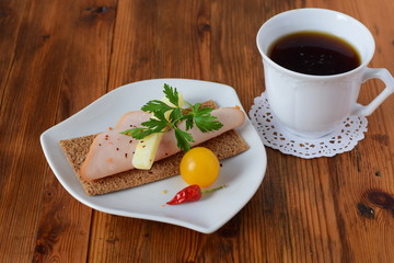 Plate with crispbread, cheese, ham, cherry tomato, cup of coffee on a wooden background. Healthy breakfast. Healthy eating concept