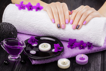 Obraz na płótnie Canvas beautiful purple manicure with violet, candle and towel on the black wooden table.
