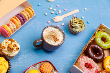 Cupcakes, macaroons and glazed donuts. Mug with whipped cream and cinnamon. Almond macaron cookies. Sweet dessert.