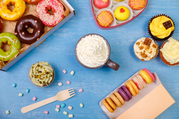 Donuts, cupcakes and macaroons. Mug with whipped cream. Cakes with buttercream. Almond macaron cookies. Sweet dessert.
