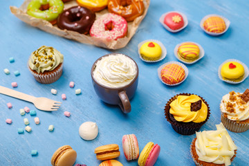 Macaroons, cupcakes and donuts. Mug with whipped cream. Almond macaron cookies with marshmallows. Sweet dessert.