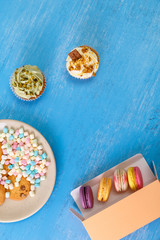 Macaroon cakes. Colored marshmallows. Cupcakes and Almond macaron cookies. Delivery box. On blue wooden rustic background.