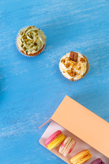 Macaroon cakes. Cupcakes with pistachio nuts cream and Almond macaron cookies. Delivery box. On blue wooden rustic background.