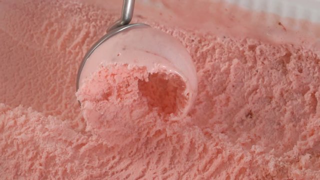 Fruit ice cream scooping out of container by metal spoon in slow motion