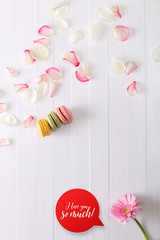 Macaroon cakes with pink rose petals and Gerbera flower. Different types of macaron. I love you speech bubble. On white wooden rustic background.