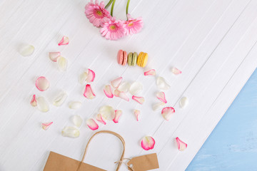 Macaroon cakes with shopping bag and Gerbera flowers. Different types of macaron. Colorful almond cookies. On white wooden rustic background.